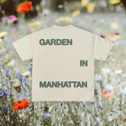 Ivory colored t-shirt with the text 'GARDEN IN MANHATTAN' printed on the front and back, displayed on a model against a floral backdrop.